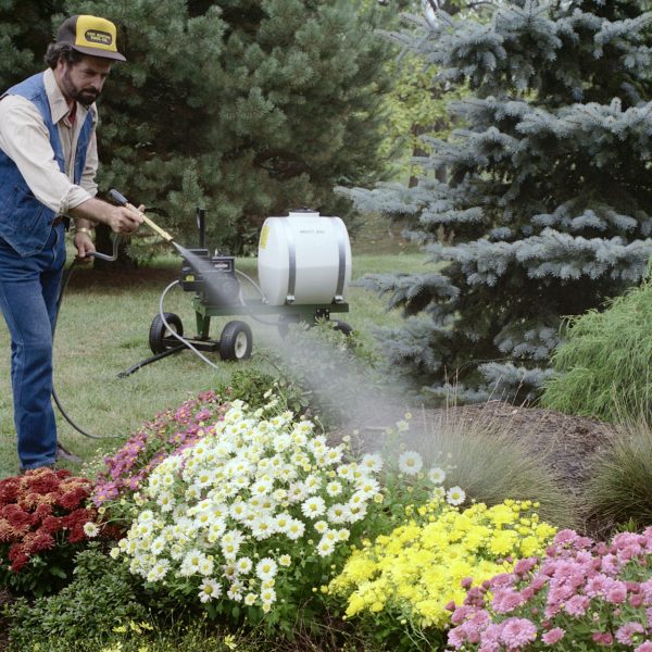 A man spraying some flowers with a Mighty Mac 22 Gallon Sprayer